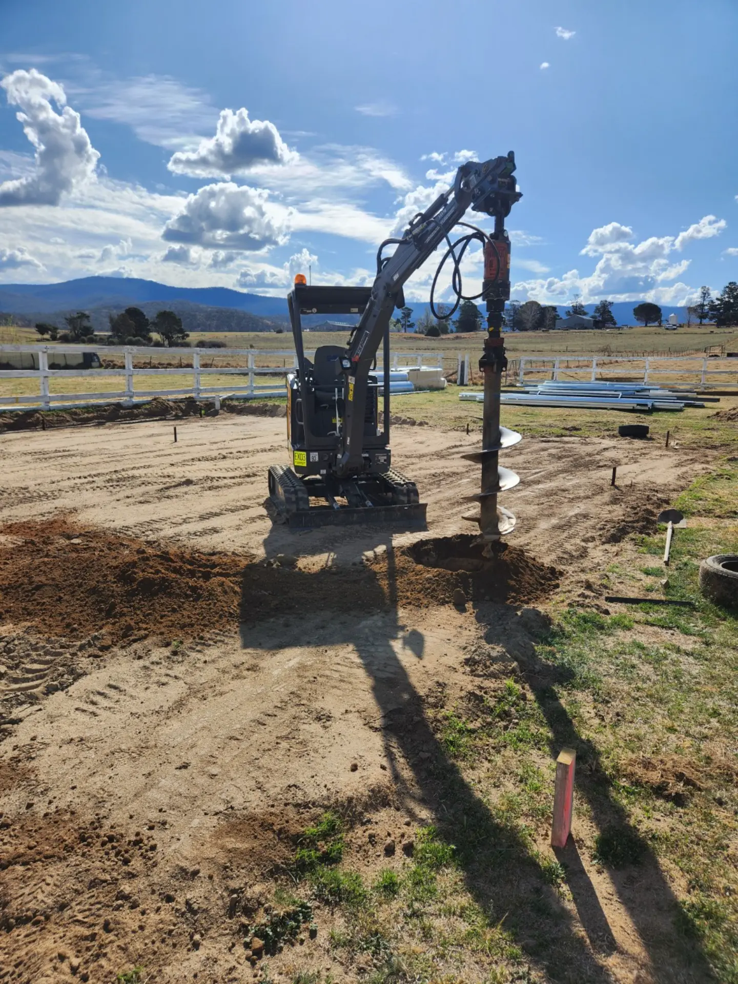 Mini excavator drilling with an auger in a rural paddock