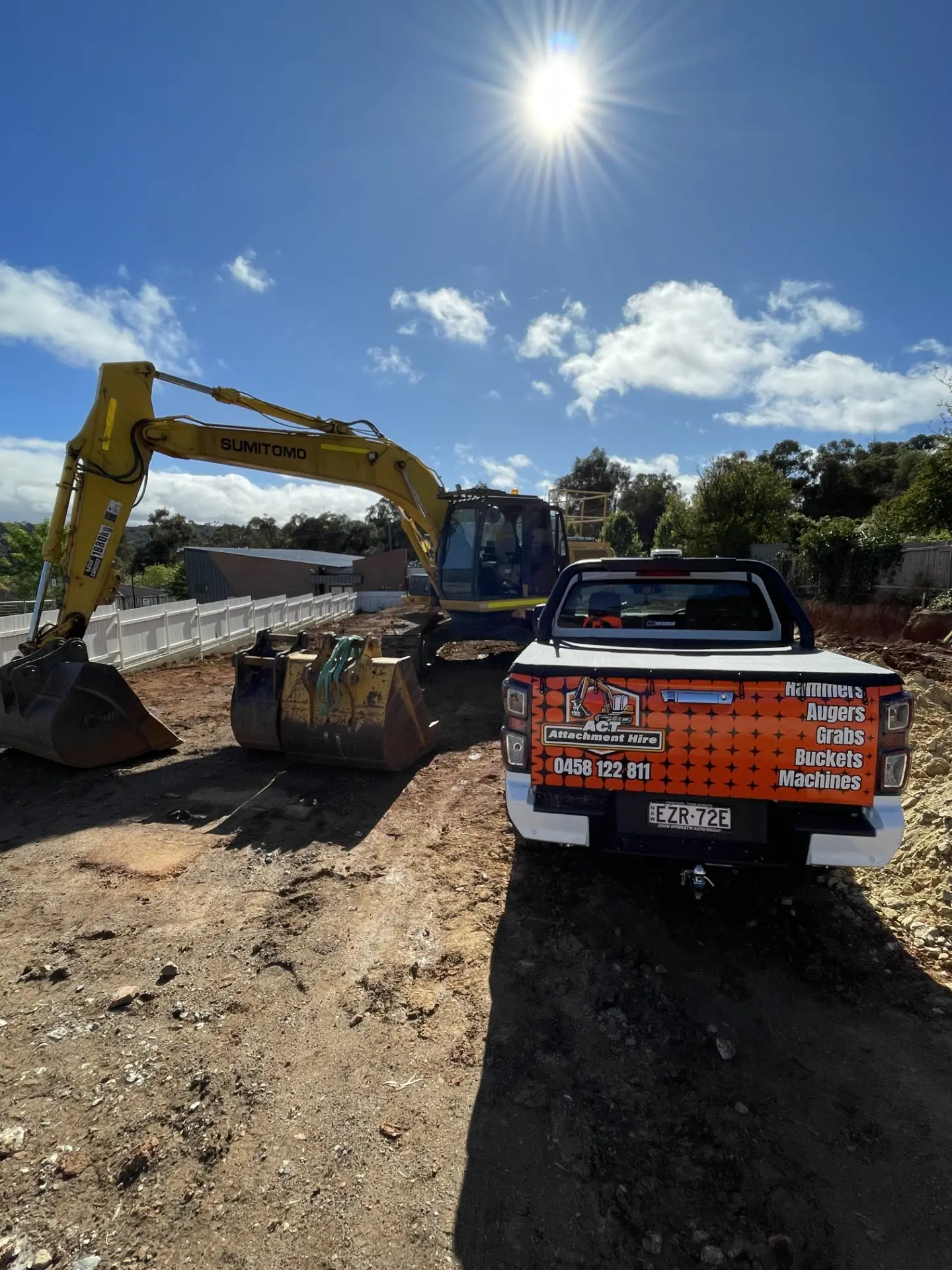 ACT Attachment Hire branded ute parked beside an excavator and spare buckets on site